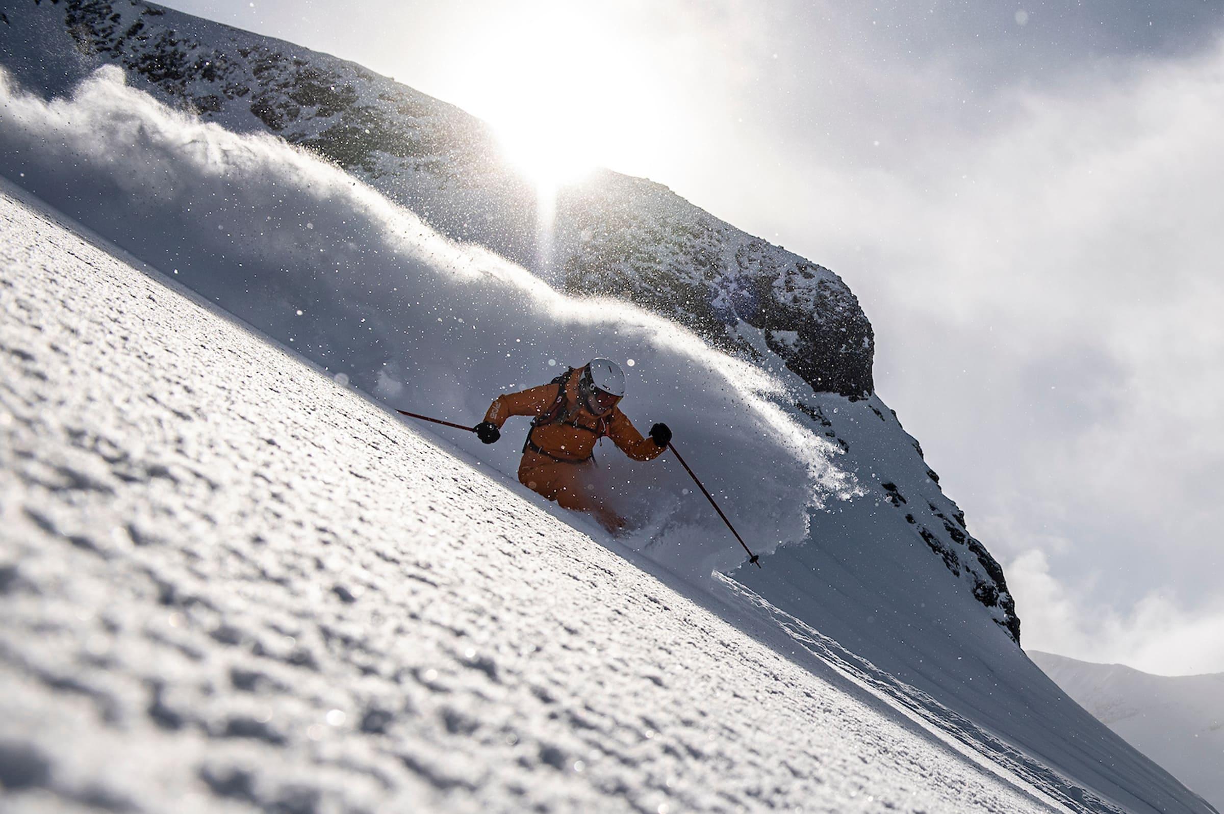 a skier in an orange jacket skis down a steep slope in waist deep powder