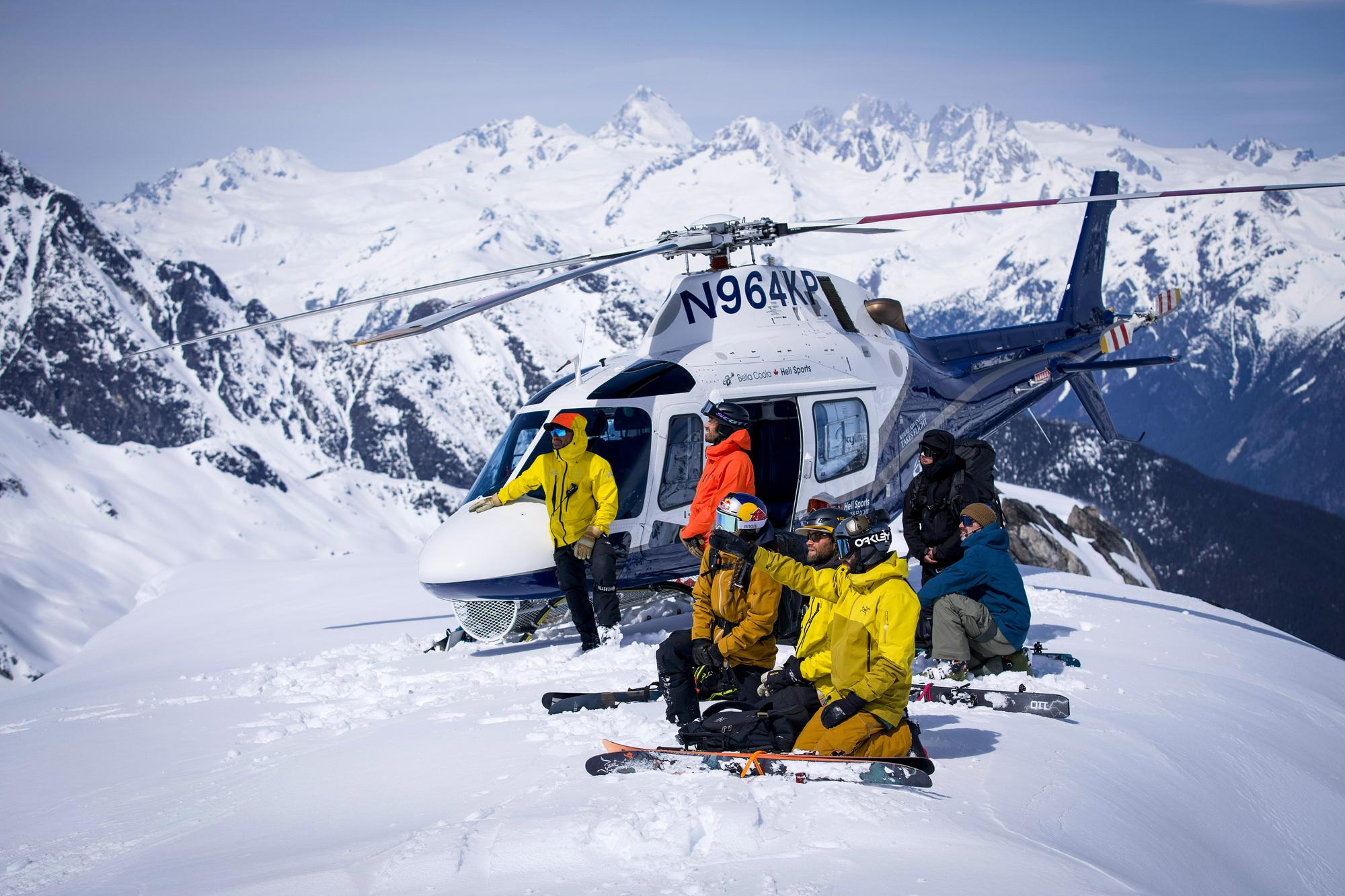 helicopter landing on a mountain top with the crew preparing to ski