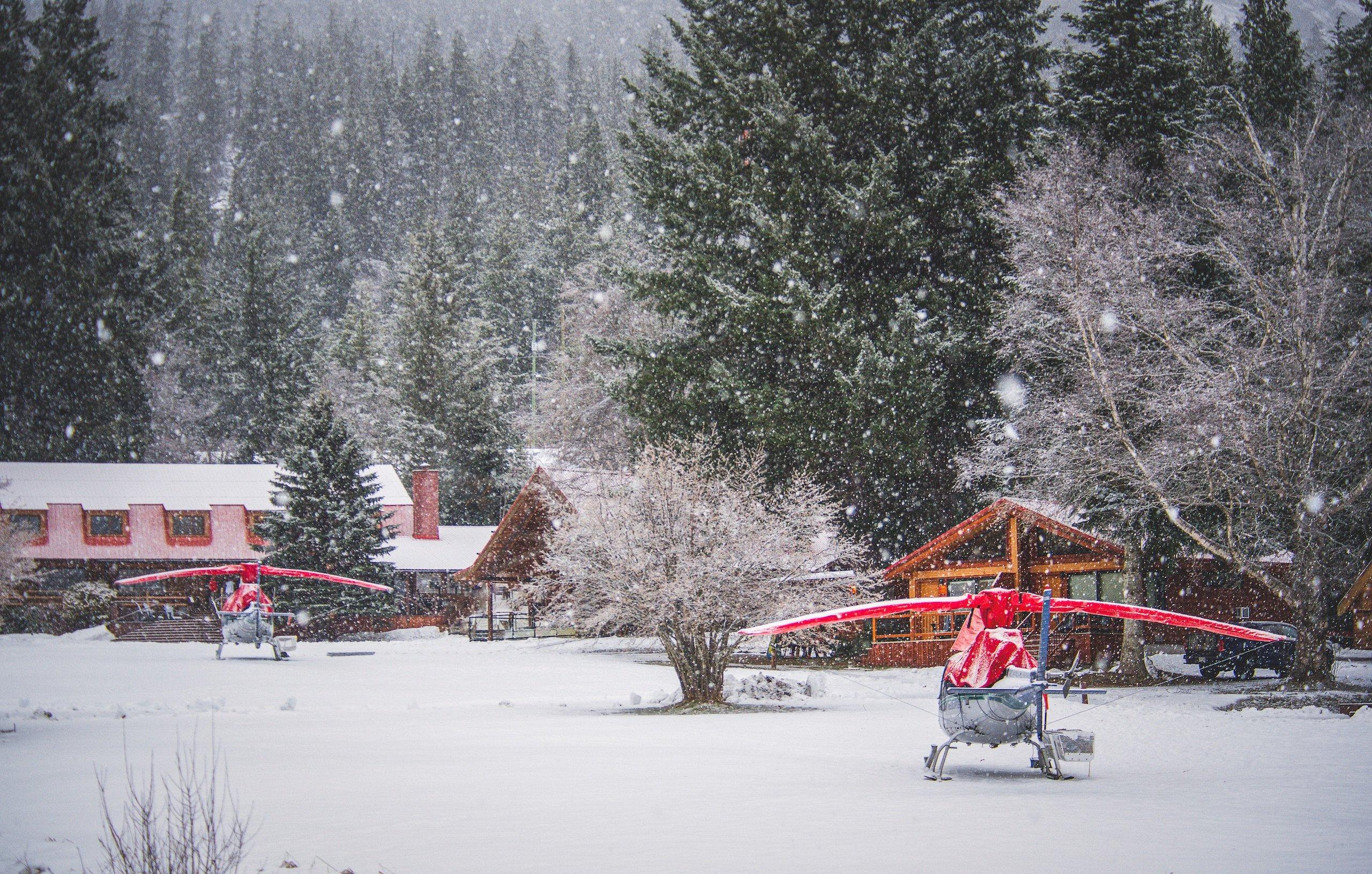 Two stationary helicopters resting on the front yard of the lodge