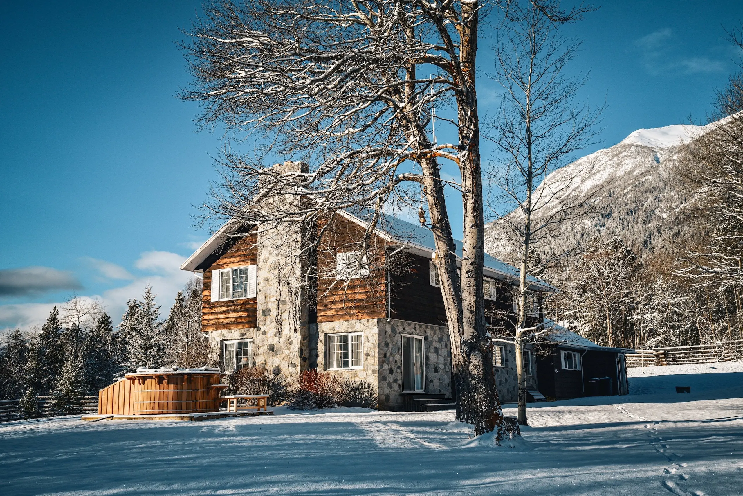 Wood and stone lodge with a hot tub and large tree in the yard