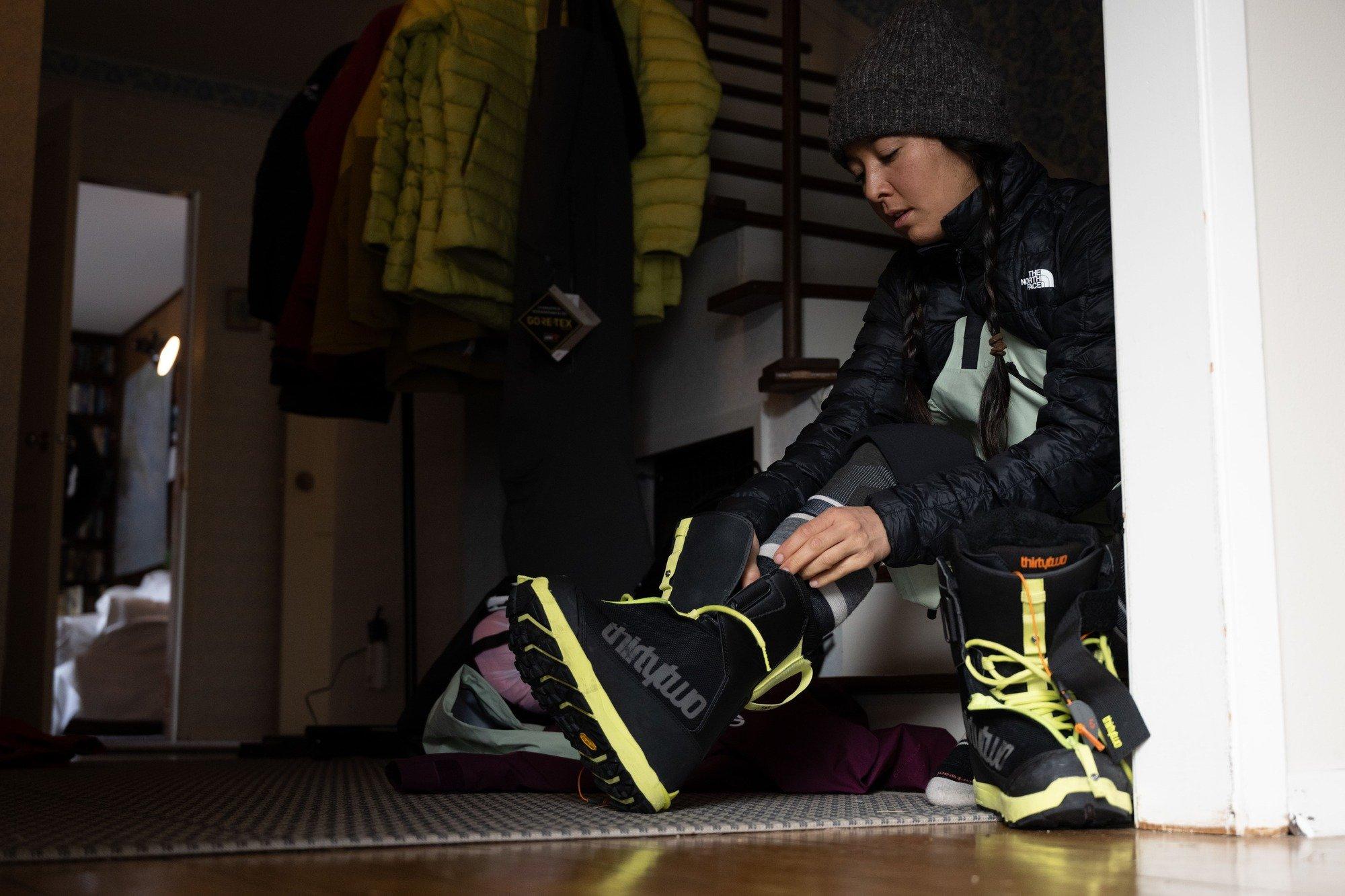 A woman putting on yellow and black snowboard boots