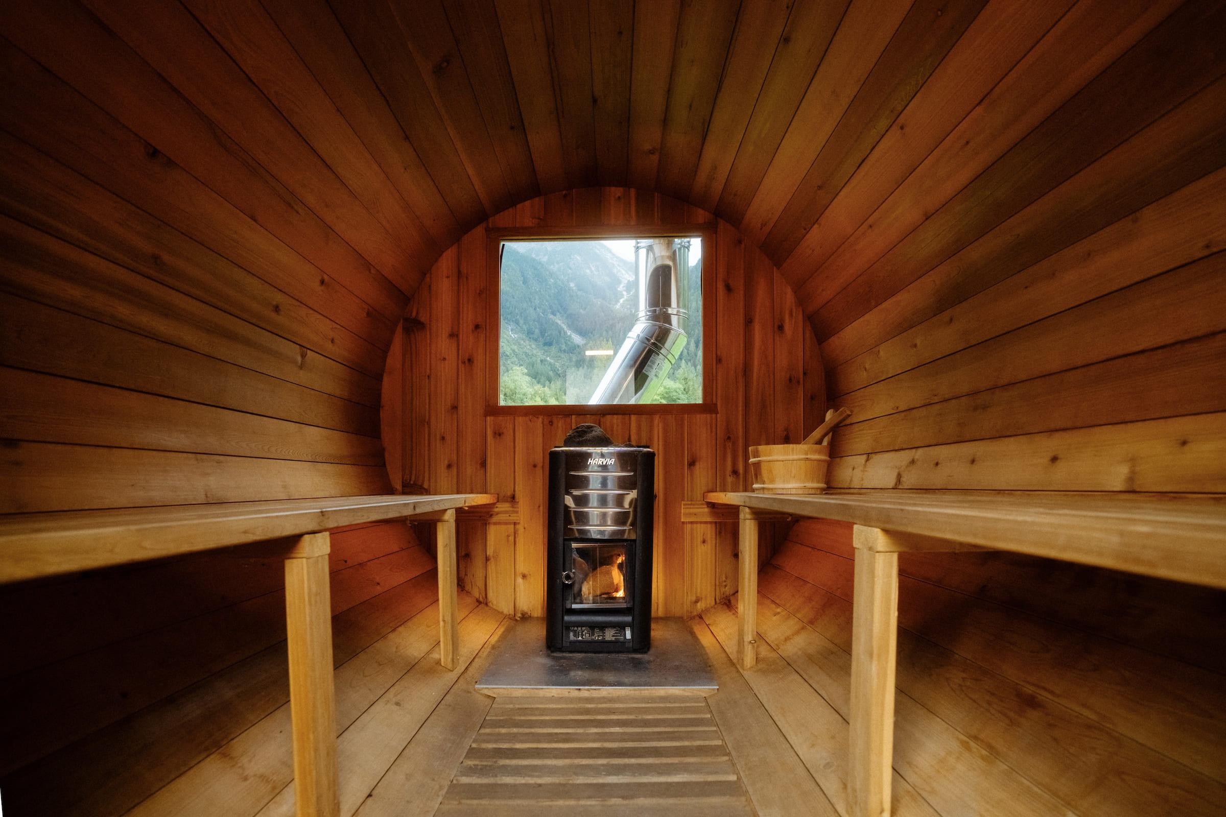 the inside of a cedar barrel sauna containing a wood fire stove and a window with mountain views