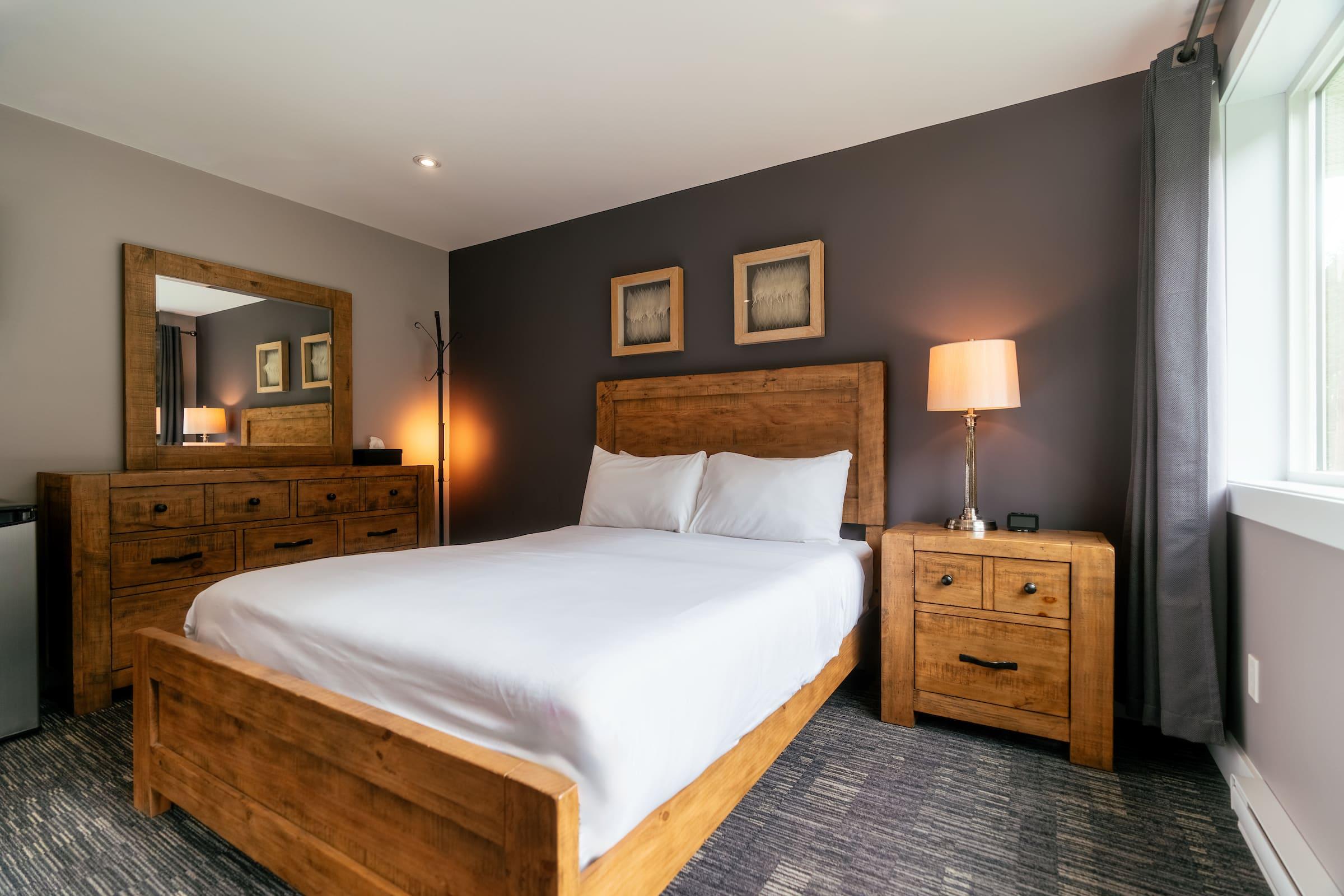 A single occupancy bedroom blue and grey wallls, a queen bed, dresser, and a nightstand with a lamp