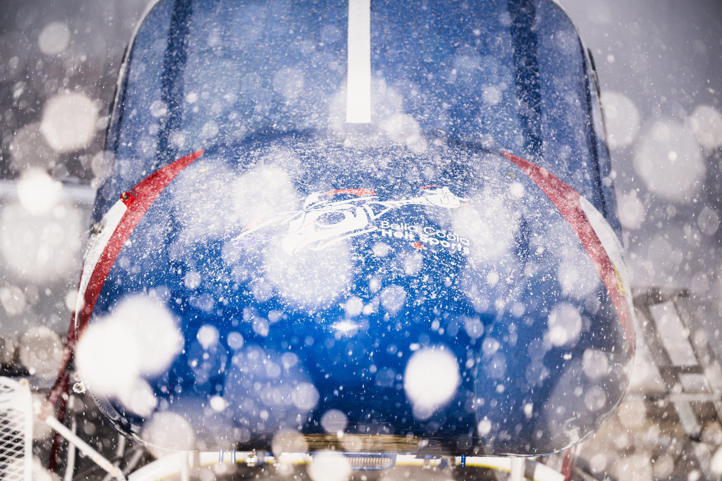 A blue Koala AW119 helicopter nose covered in snowflakes, focusing on the logo against a snowy background.