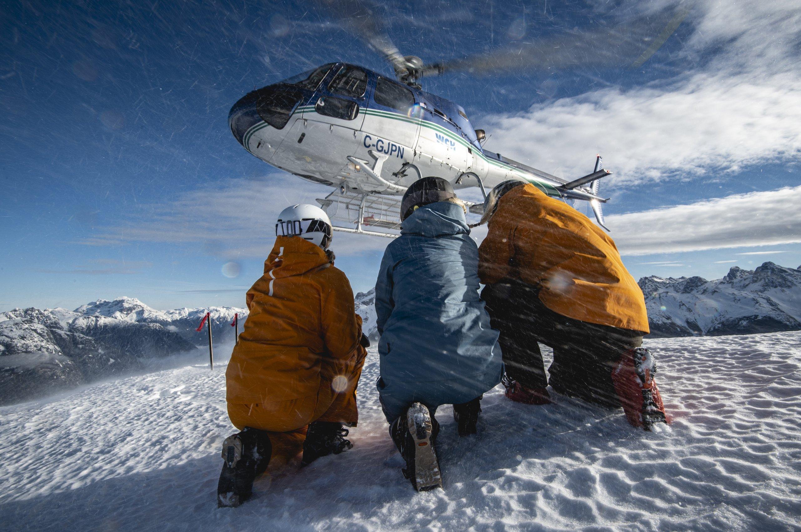 a group of skier kneeling as a helicopter takes off in front of them